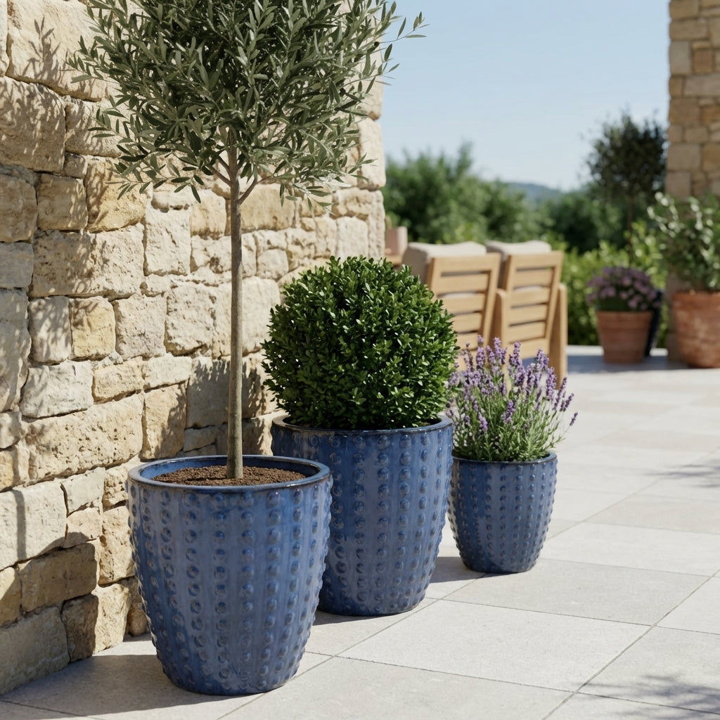 Detail na ručně vyráběný keramický květináč Attila Anticky modrá z terakoty s lesklou glazurou a reliéfem na slunné kamenné dlažbě.