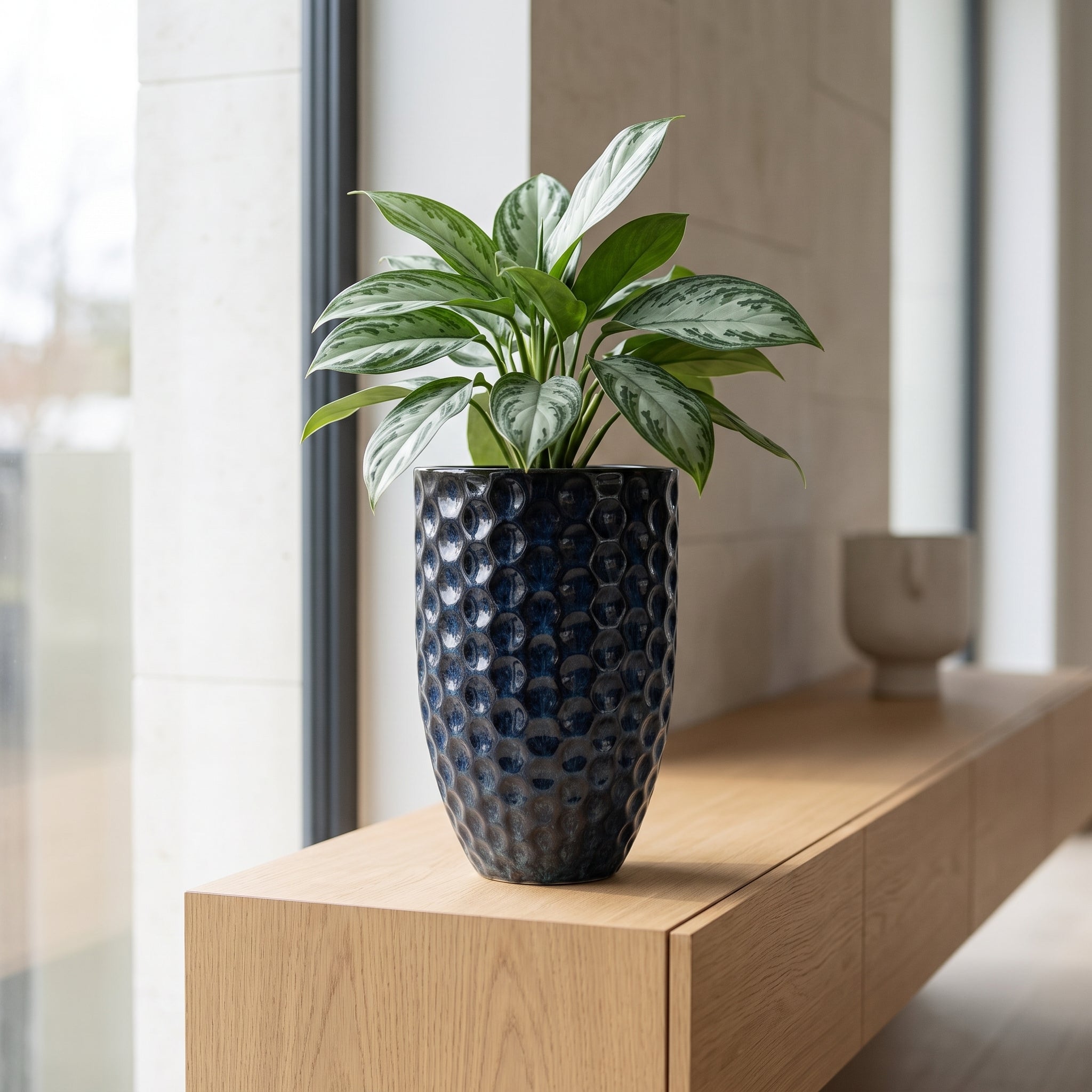 Keramický květináč MEROVEE M (23x35 cm) v ledově modré barvě s rostlinou Aglaonema na dřevěné polici v luxusním skandinávském interiéru.