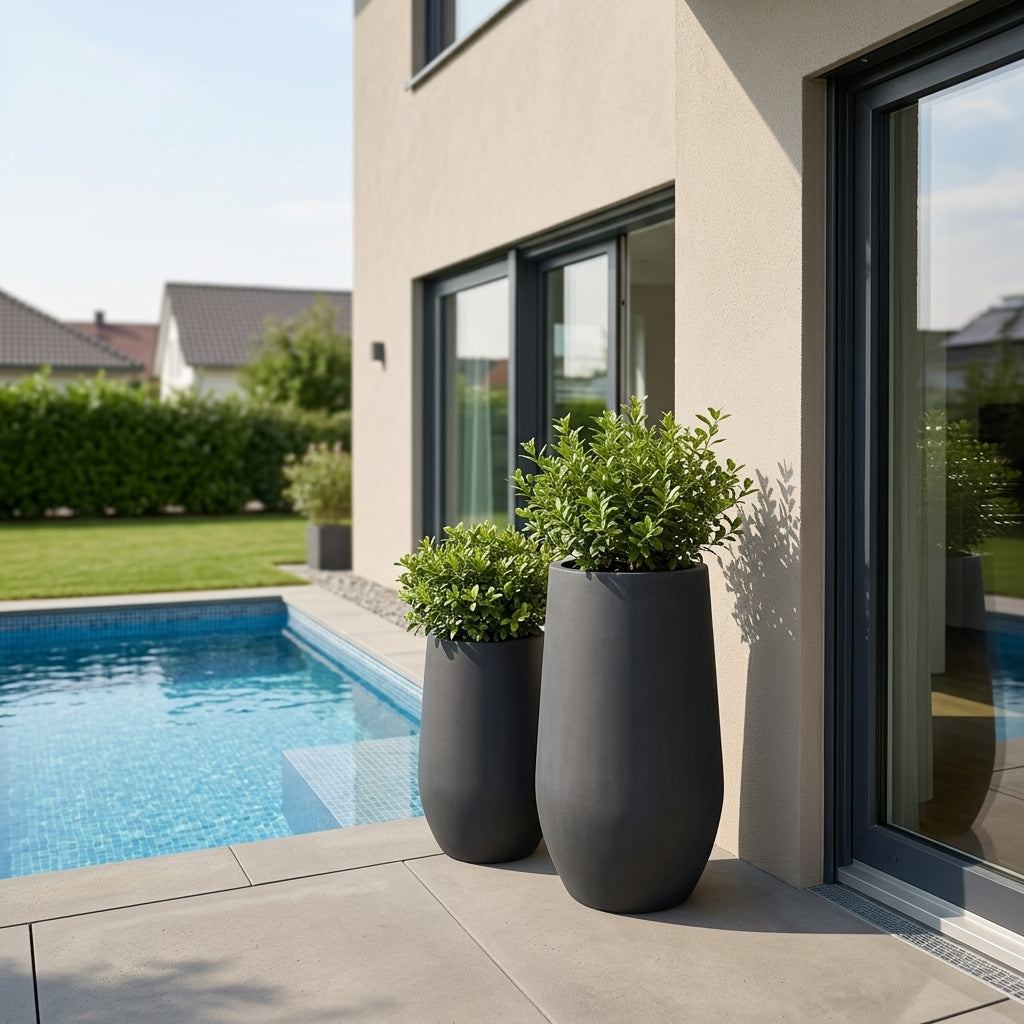Detailní pohled na matně černý betonový květináč Zenith XL s keřem na moderní rodinné terase u bazénu.