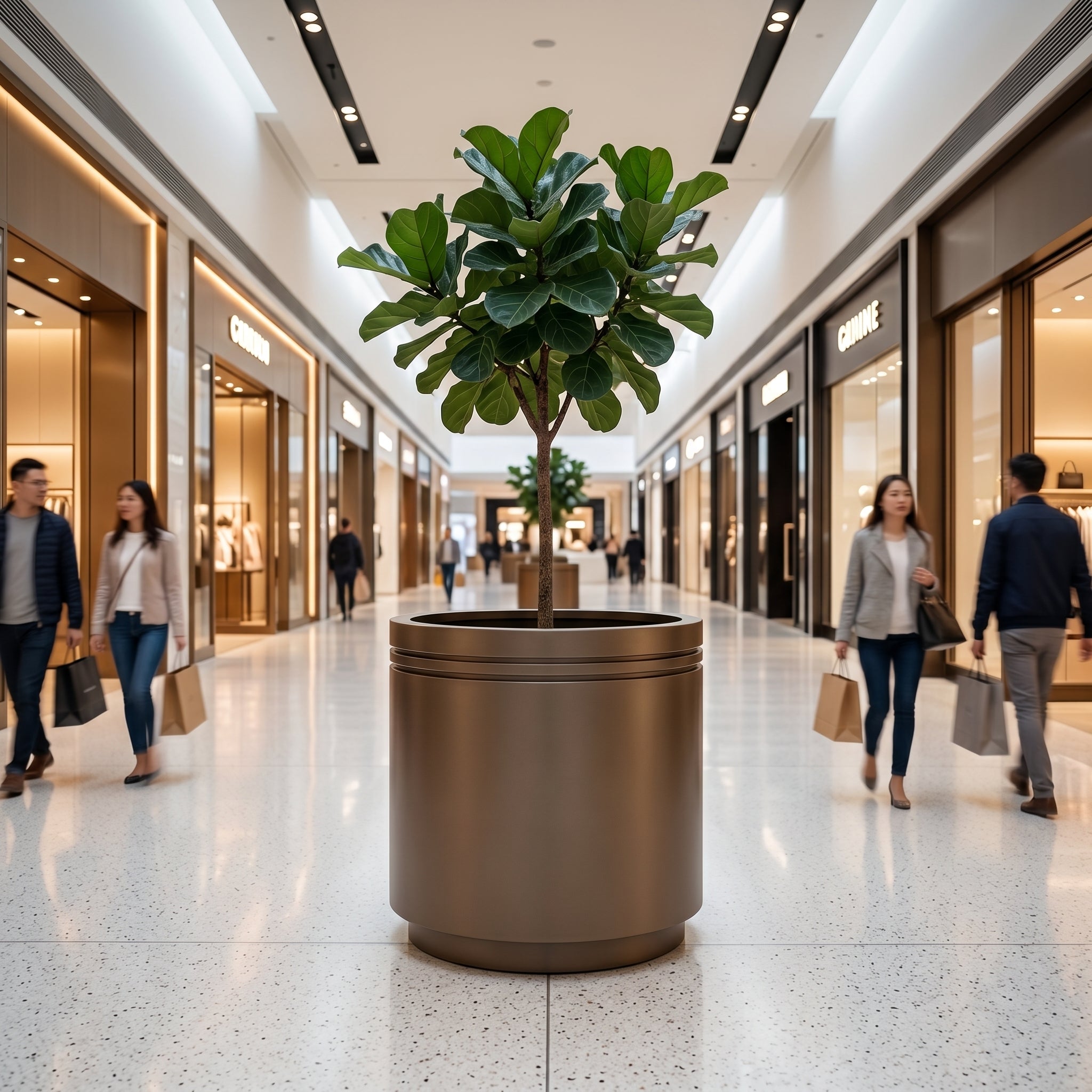 Velký pozinkovaný ocelový květináč INFINITY ROUND šedohnědá XL s rostlinou Ficus lyrata v chodbě moderního nákupního centra.