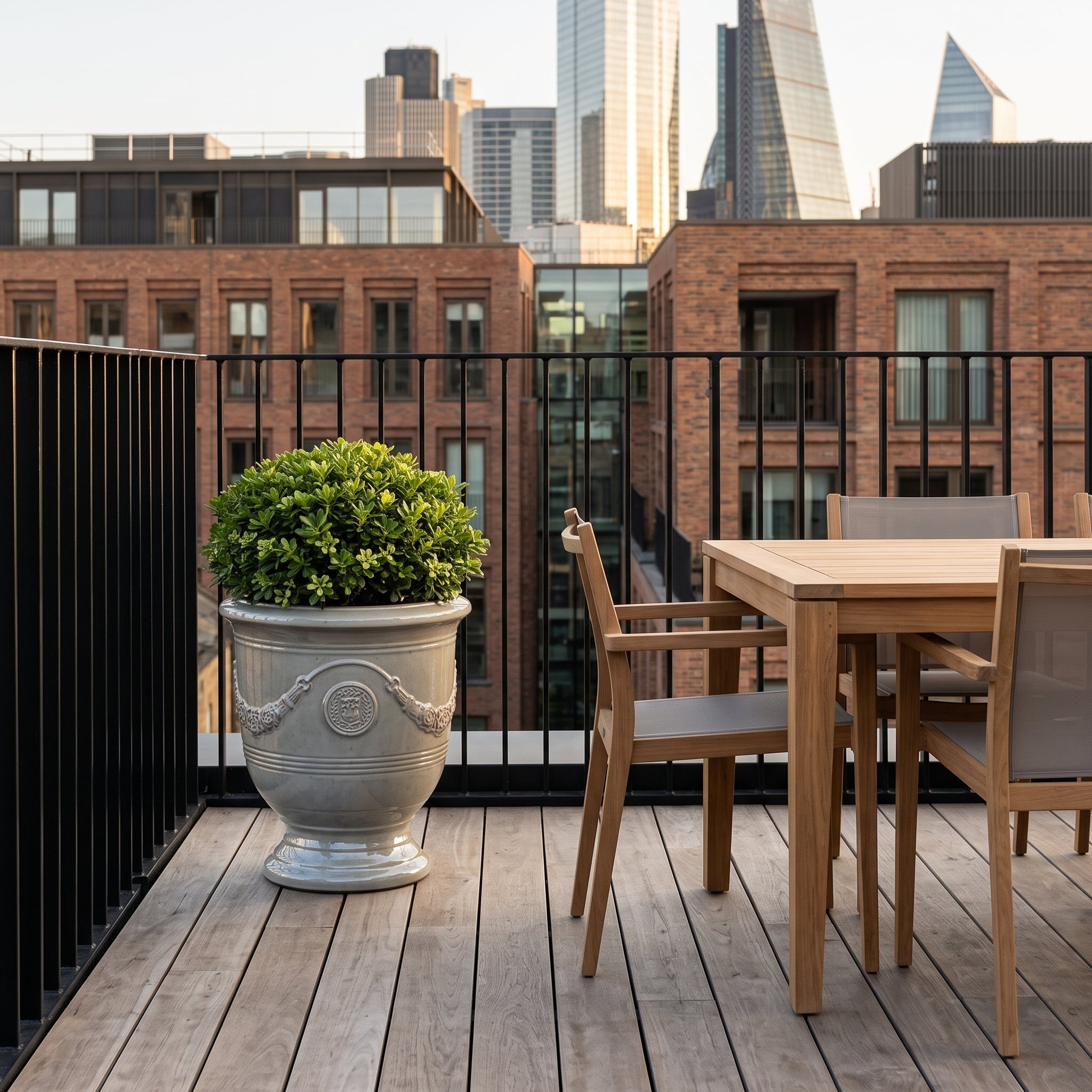 Keramický květináč RICHELIEU - Perlová - XL (46 x 56 cm) s kompaktním keřem na moderní střešní terase vedle teakového stolu.