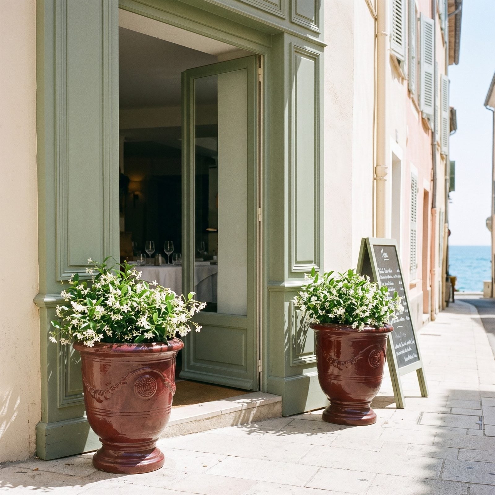 Zwei Pflanzkübel RICHELIEU Ziegelrot mit Olivenbäumen beidseits einer Hoteltür an der Riviera